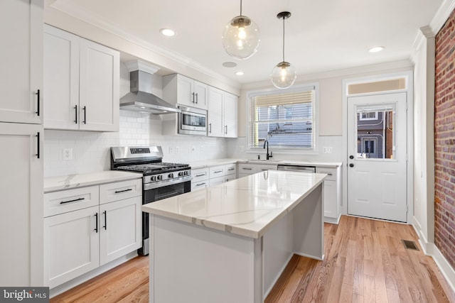 kitchen with white cabinetry, appliances with stainless steel finishes, pendant lighting, wall chimney exhaust hood, and a center island