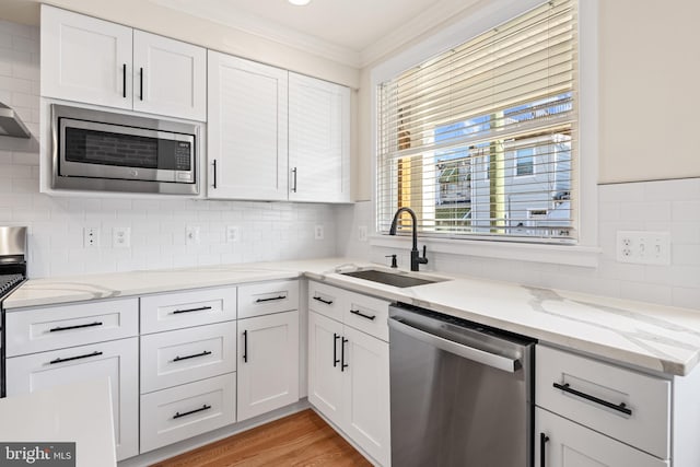 kitchen with white cabinetry, stainless steel appliances, tasteful backsplash, sink, and light wood-type flooring