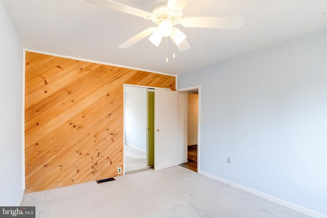 unfurnished bedroom with ceiling fan, light colored carpet, wooden walls, and a closet