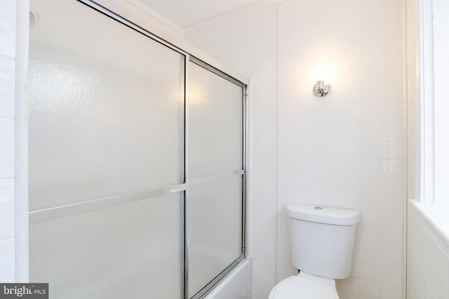 bathroom with tile walls, crown molding, enclosed tub / shower combo, and toilet