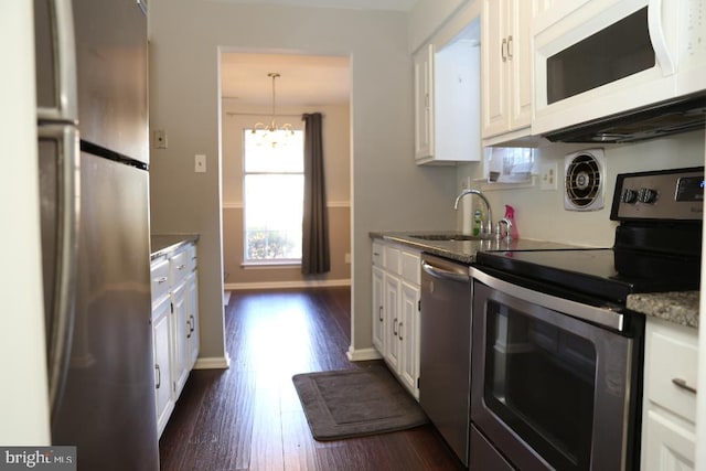 kitchen featuring dark wood-type flooring, hanging light fixtures, sink, appliances with stainless steel finishes, and white cabinetry