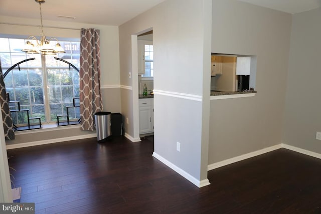 spare room featuring a chandelier, dark hardwood / wood-style flooring, and a healthy amount of sunlight