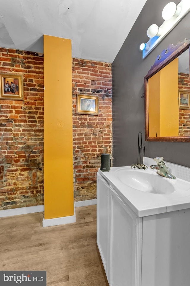 bathroom featuring hardwood / wood-style floors, vanity, and brick wall