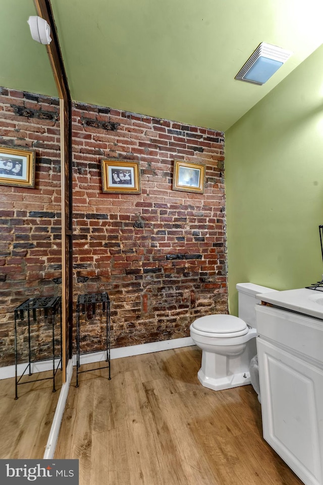 bathroom featuring hardwood / wood-style floors, vanity, toilet, and brick wall