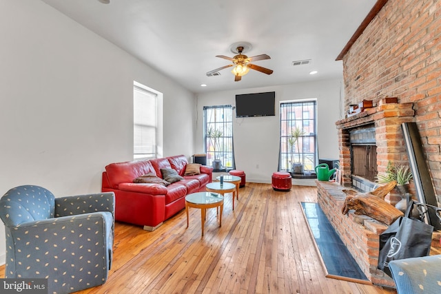 living room featuring a brick fireplace, ceiling fan, and light hardwood / wood-style flooring