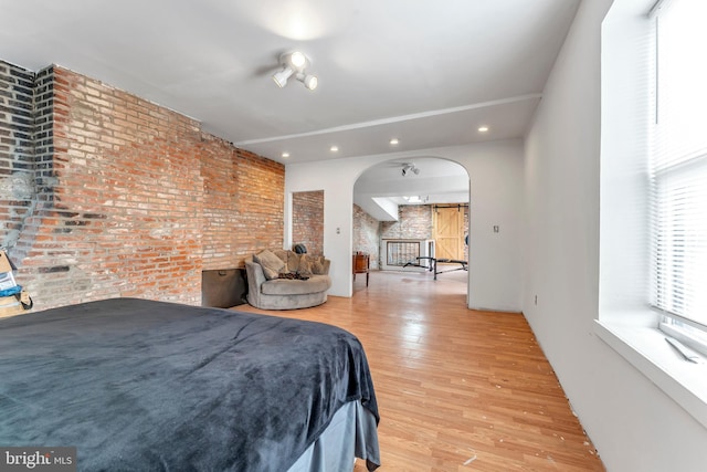 bedroom with a barn door, light hardwood / wood-style flooring, and brick wall