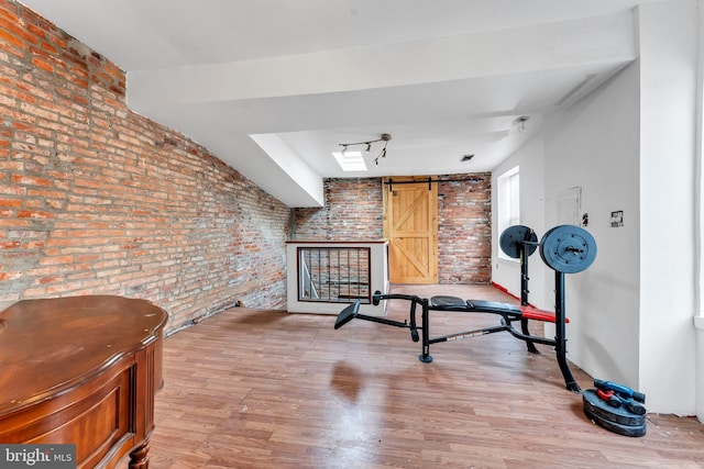 workout area with a barn door, brick wall, and light wood-type flooring