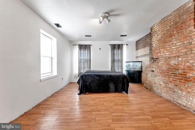 bedroom featuring light wood-type flooring and brick wall