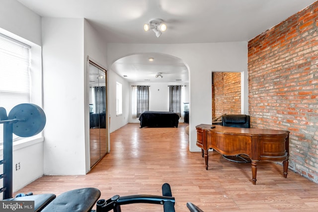 workout room featuring light hardwood / wood-style flooring, ceiling fan, and brick wall