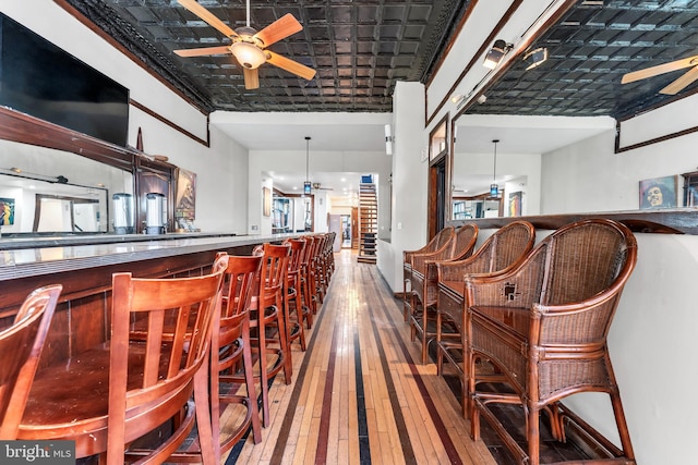 bar featuring hardwood / wood-style flooring, ceiling fan, crown molding, and hanging light fixtures