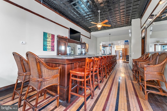 bar featuring a towering ceiling, hardwood / wood-style flooring, ceiling fan, and crown molding