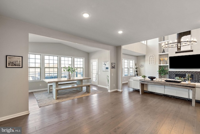 interior space with a tiled fireplace, wood-type flooring, lofted ceiling, and a notable chandelier