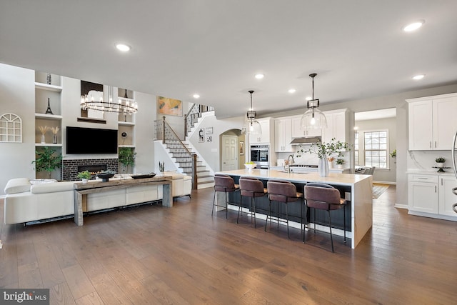 kitchen with white cabinetry, dark hardwood / wood-style flooring, hanging light fixtures, and a center island with sink