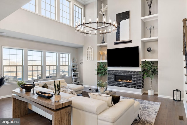 living room with dark hardwood / wood-style flooring, an inviting chandelier, built in features, a fireplace, and a high ceiling