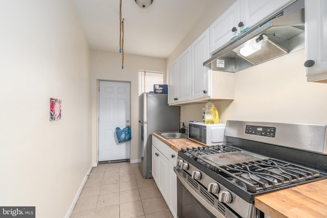 kitchen with sink, light tile patterned floors, stainless steel gas range, butcher block countertops, and white cabinetry