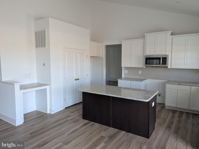 kitchen featuring wood finished floors, white cabinetry, visible vents, light stone countertops, and stainless steel microwave