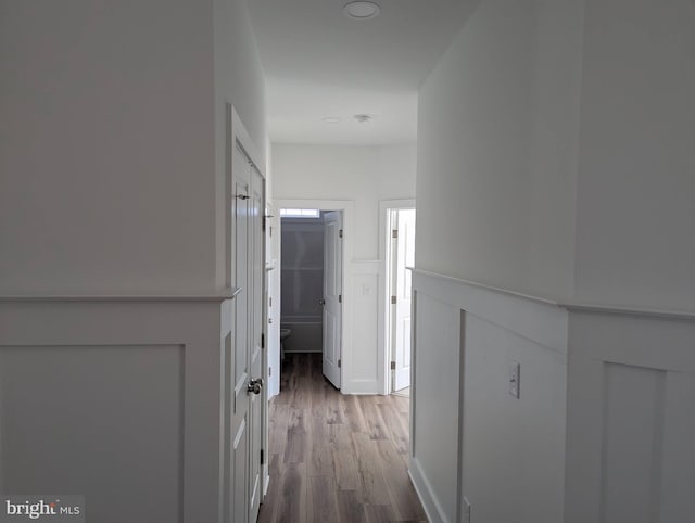 corridor with light wood-style floors, a decorative wall, and a wainscoted wall