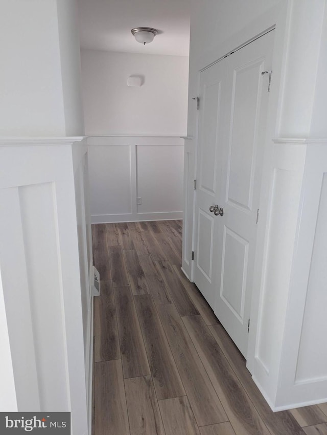 corridor with dark wood-style floors, a wainscoted wall, and a decorative wall