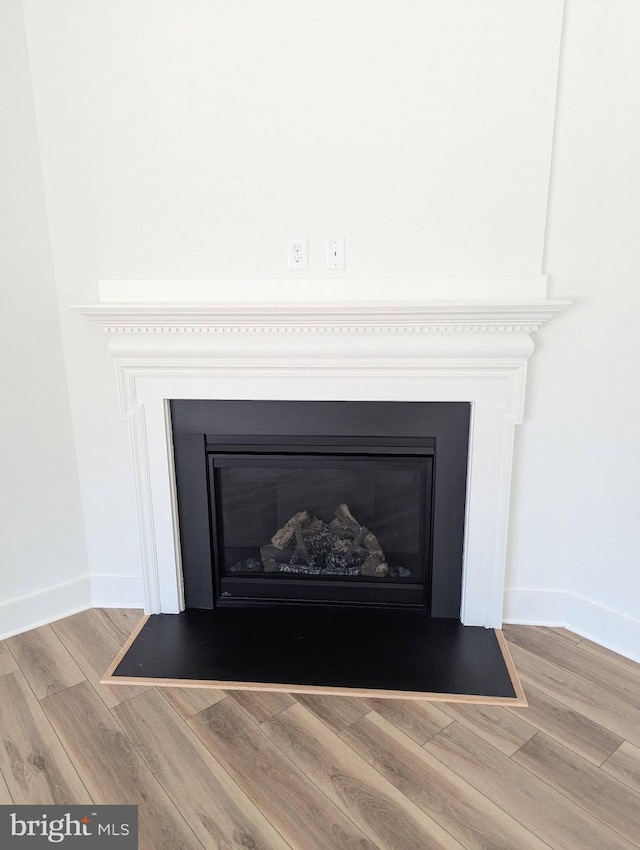 room details featuring a fireplace with flush hearth, baseboards, and wood finished floors