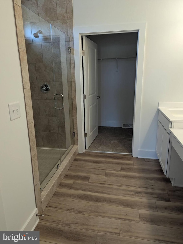 bathroom with visible vents, wood finished floors, a spacious closet, vanity, and a shower stall