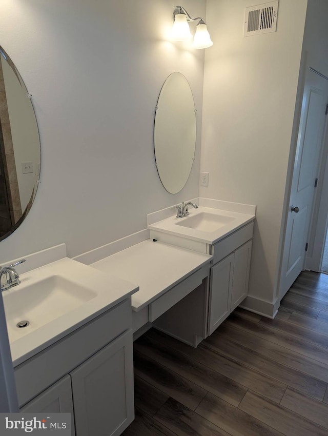 full bath featuring wood finished floors, two vanities, a sink, and visible vents