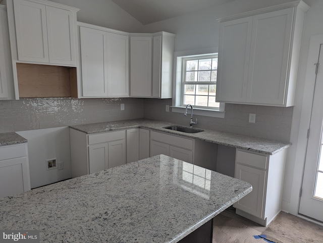 kitchen with white cabinetry, a sink, backsplash, and light stone countertops