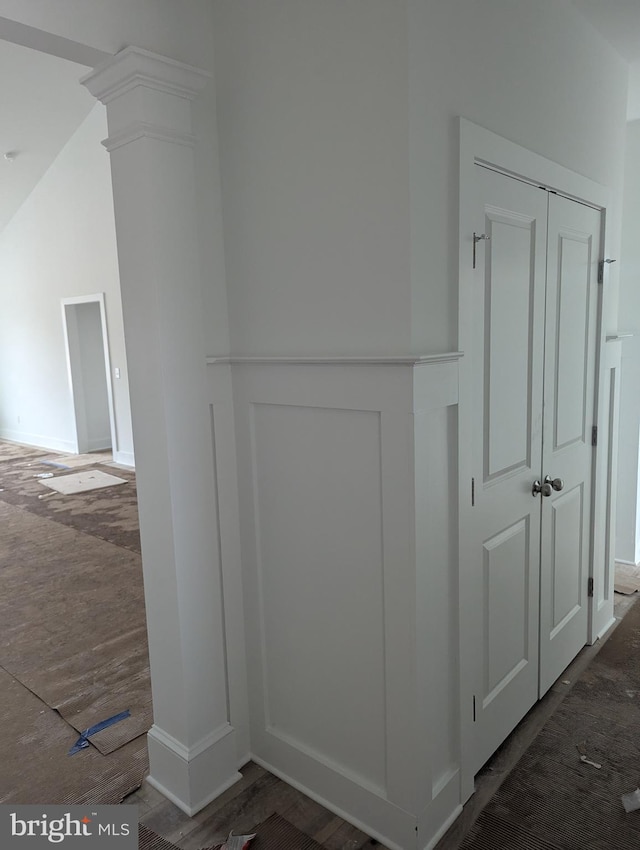 hallway featuring lofted ceiling, wood finished floors, and decorative columns