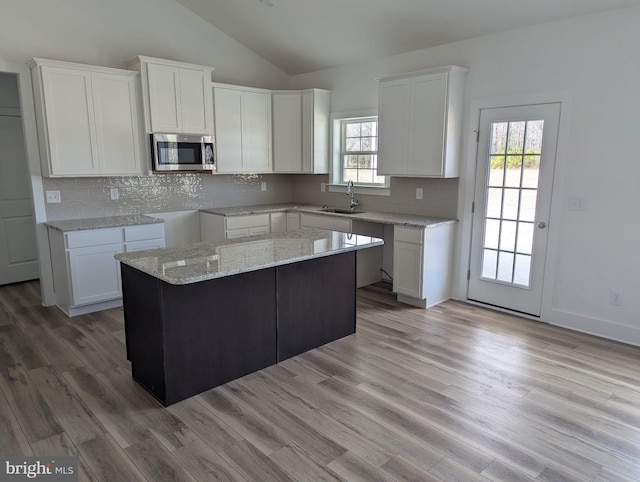 kitchen featuring a sink, white cabinets, vaulted ceiling, light wood-style floors, and stainless steel microwave