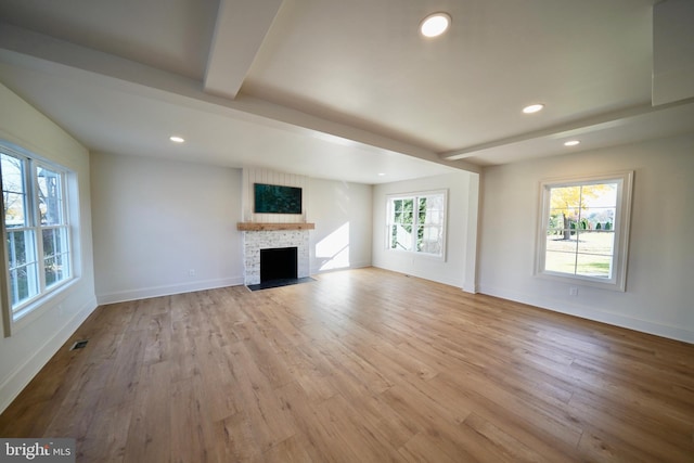 unfurnished living room featuring a stone fireplace, plenty of natural light, and light wood-type flooring