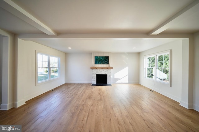 unfurnished living room with a fireplace, beam ceiling, light hardwood / wood-style flooring, and a healthy amount of sunlight