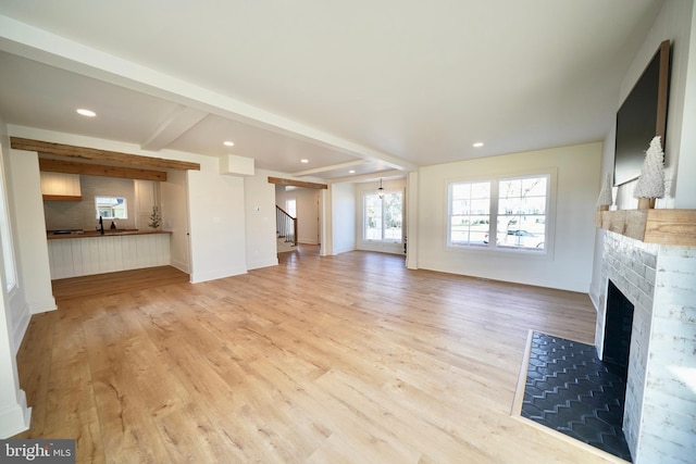 unfurnished living room with beam ceiling, light hardwood / wood-style flooring, and sink