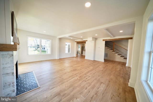 unfurnished living room featuring beam ceiling and light hardwood / wood-style floors