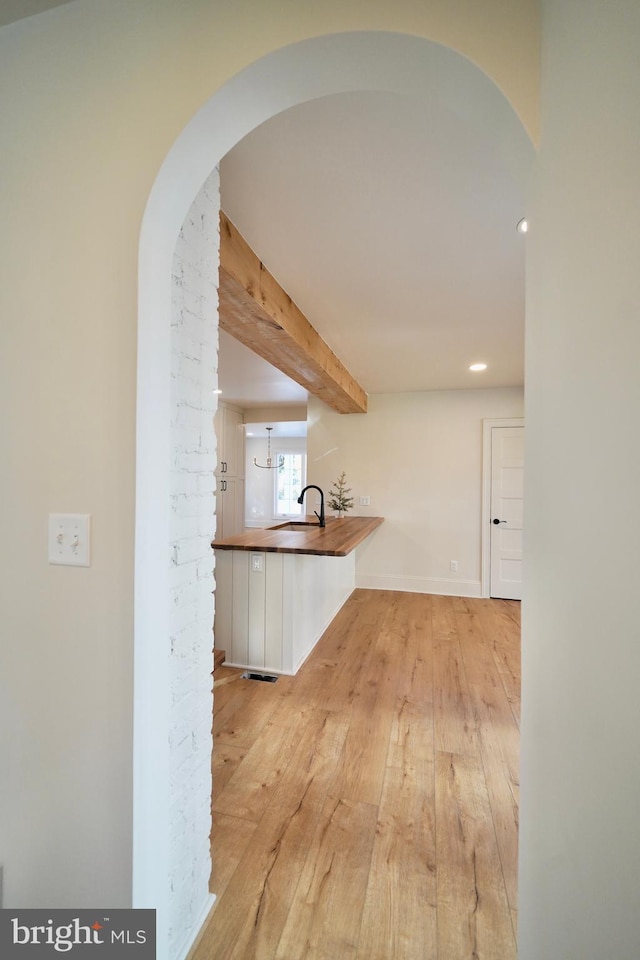 hallway featuring beamed ceiling, light hardwood / wood-style floors, and sink