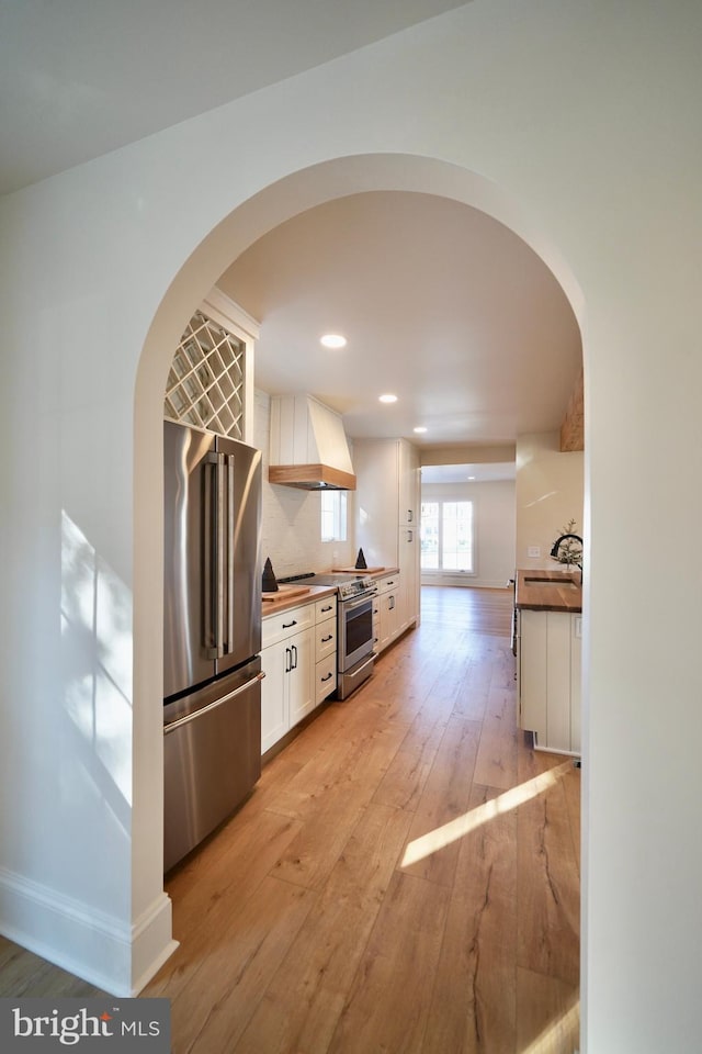 kitchen with appliances with stainless steel finishes, tasteful backsplash, premium range hood, light hardwood / wood-style floors, and white cabinetry