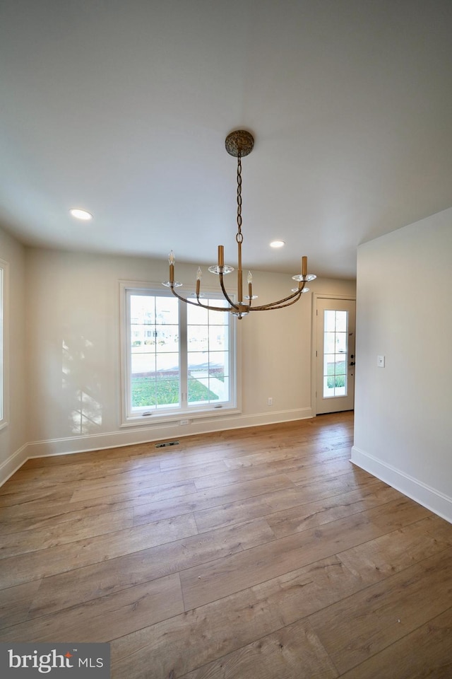 unfurnished dining area with a wealth of natural light, a notable chandelier, and light wood-type flooring