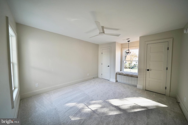 unfurnished bedroom featuring ceiling fan with notable chandelier and light colored carpet