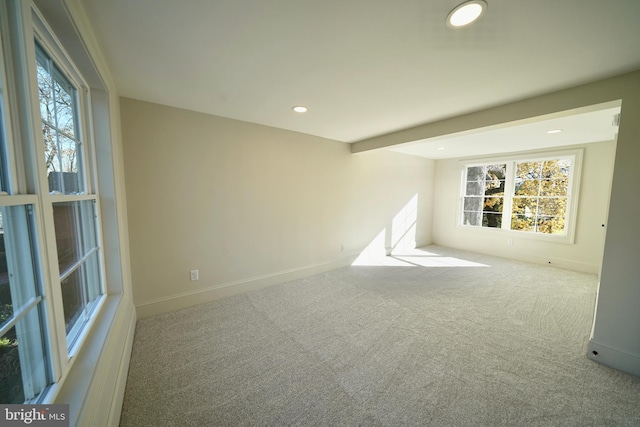 spare room featuring beam ceiling, light colored carpet, and plenty of natural light