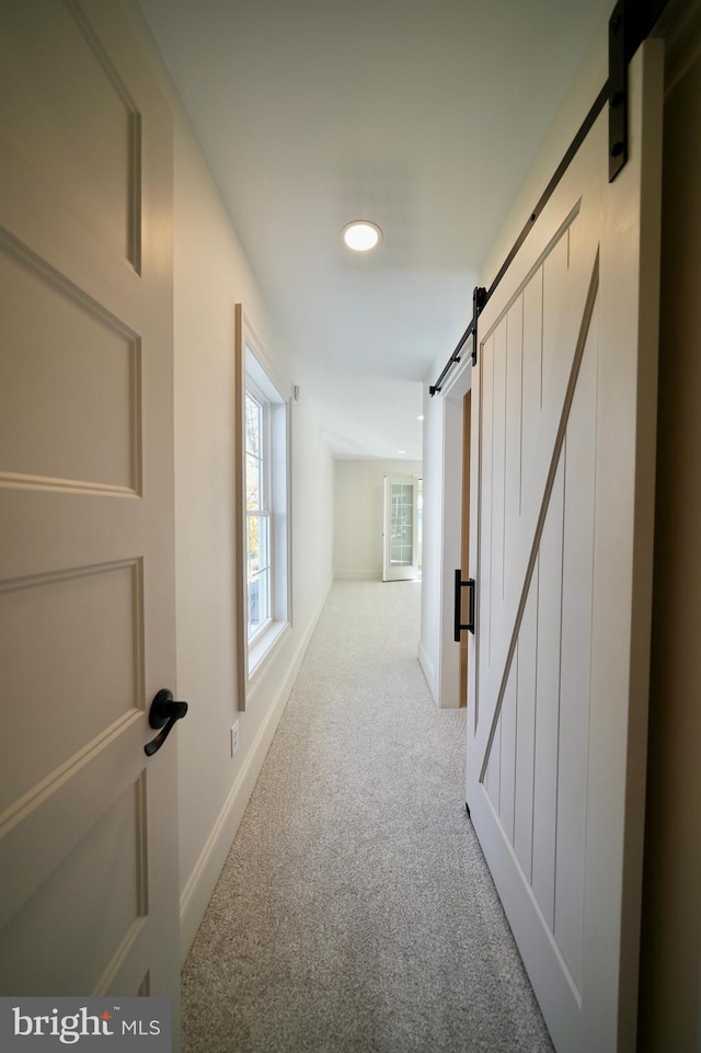 hallway with a barn door and light colored carpet