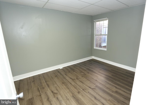 spare room featuring a drop ceiling and dark wood-type flooring