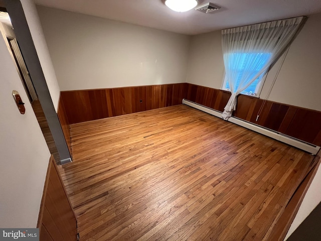 unfurnished room featuring hardwood / wood-style flooring, a baseboard radiator, and wooden walls