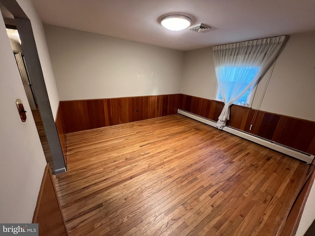 spare room with light hardwood / wood-style floors, baseboard heating, and wooden walls