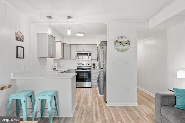 kitchen with sink, light hardwood / wood-style floors, a kitchen bar, kitchen peninsula, and stainless steel appliances