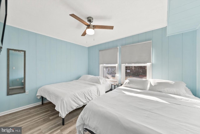 bedroom with ceiling fan, hardwood / wood-style floors, and wooden walls