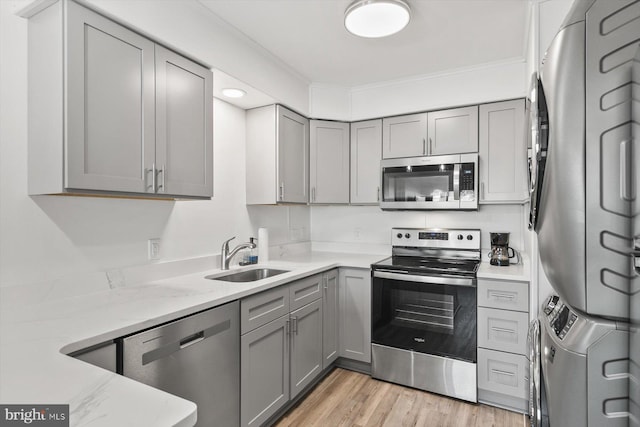 kitchen with appliances with stainless steel finishes, light stone counters, sink, light hardwood / wood-style flooring, and stacked washer and clothes dryer