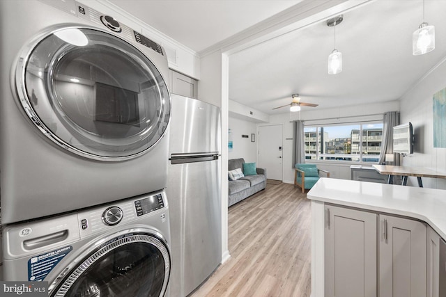 clothes washing area with crown molding, ceiling fan, stacked washer and clothes dryer, and light wood-type flooring