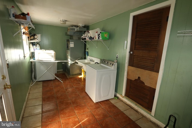 clothes washing area with washer and dryer, sink, dark tile patterned flooring, and wooden walls