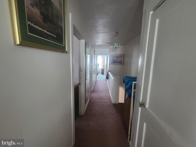 hall with dark colored carpet and a chandelier