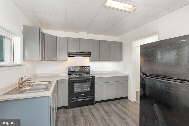 kitchen featuring sink, a paneled ceiling, gray cabinets, black appliances, and hardwood / wood-style flooring