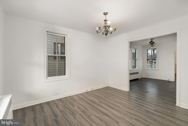 spare room featuring ceiling fan with notable chandelier, dark wood-type flooring, and radiator