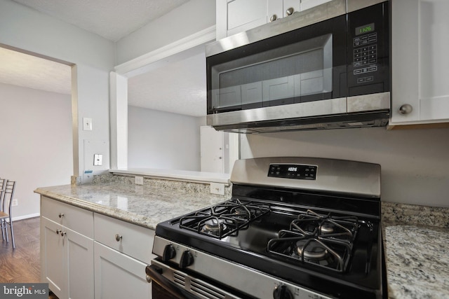 kitchen with light stone countertops, dark wood-type flooring, black gas stove, a textured ceiling, and white cabinets